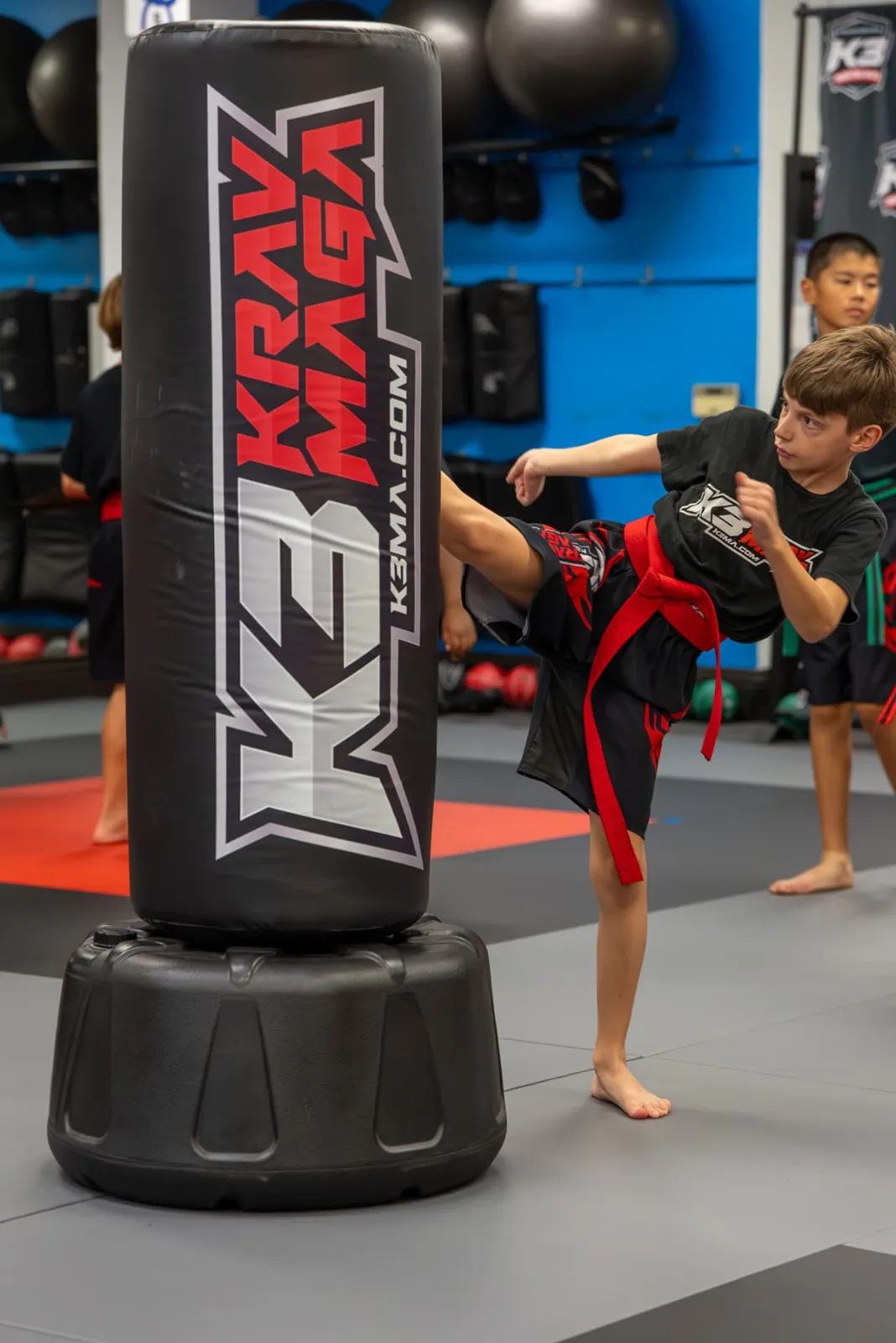 Boy with a red belt kicking the heavy bag